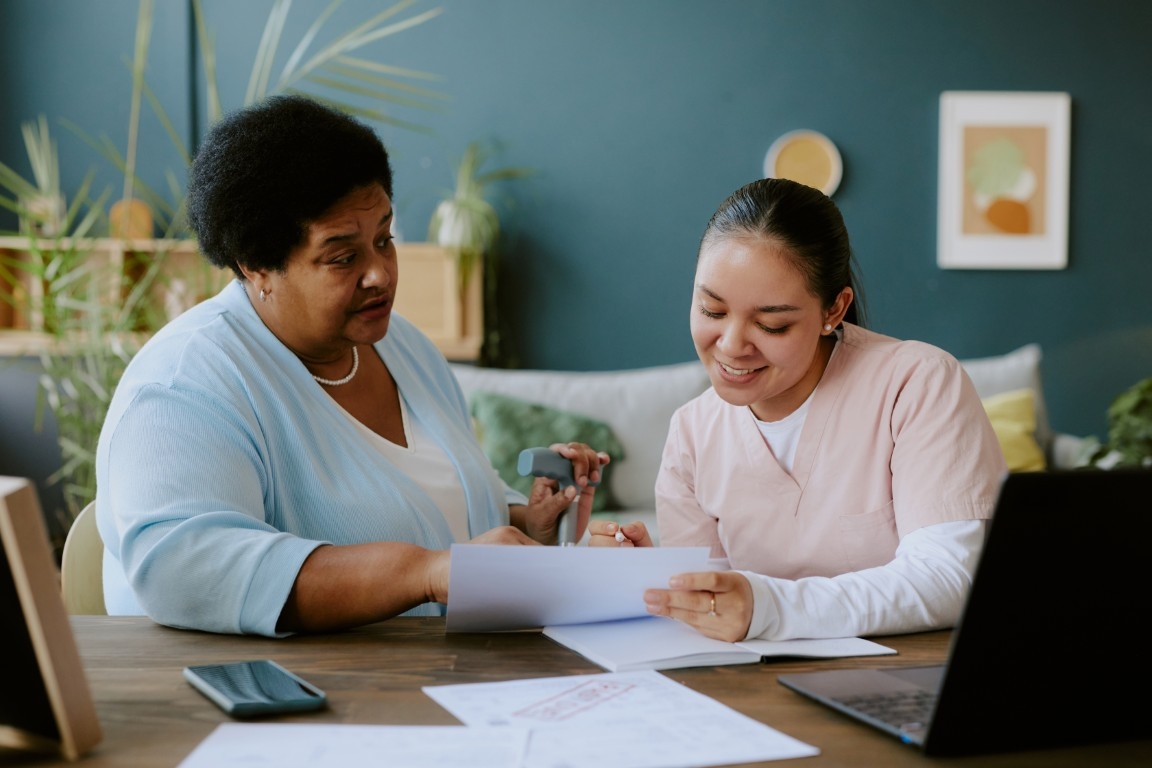 A carer sat at a table with an elderly woman looking at paperwork