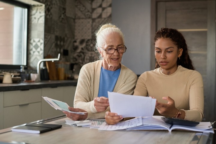 A young woman sitting next to her elderly relative at a table looking at documents
